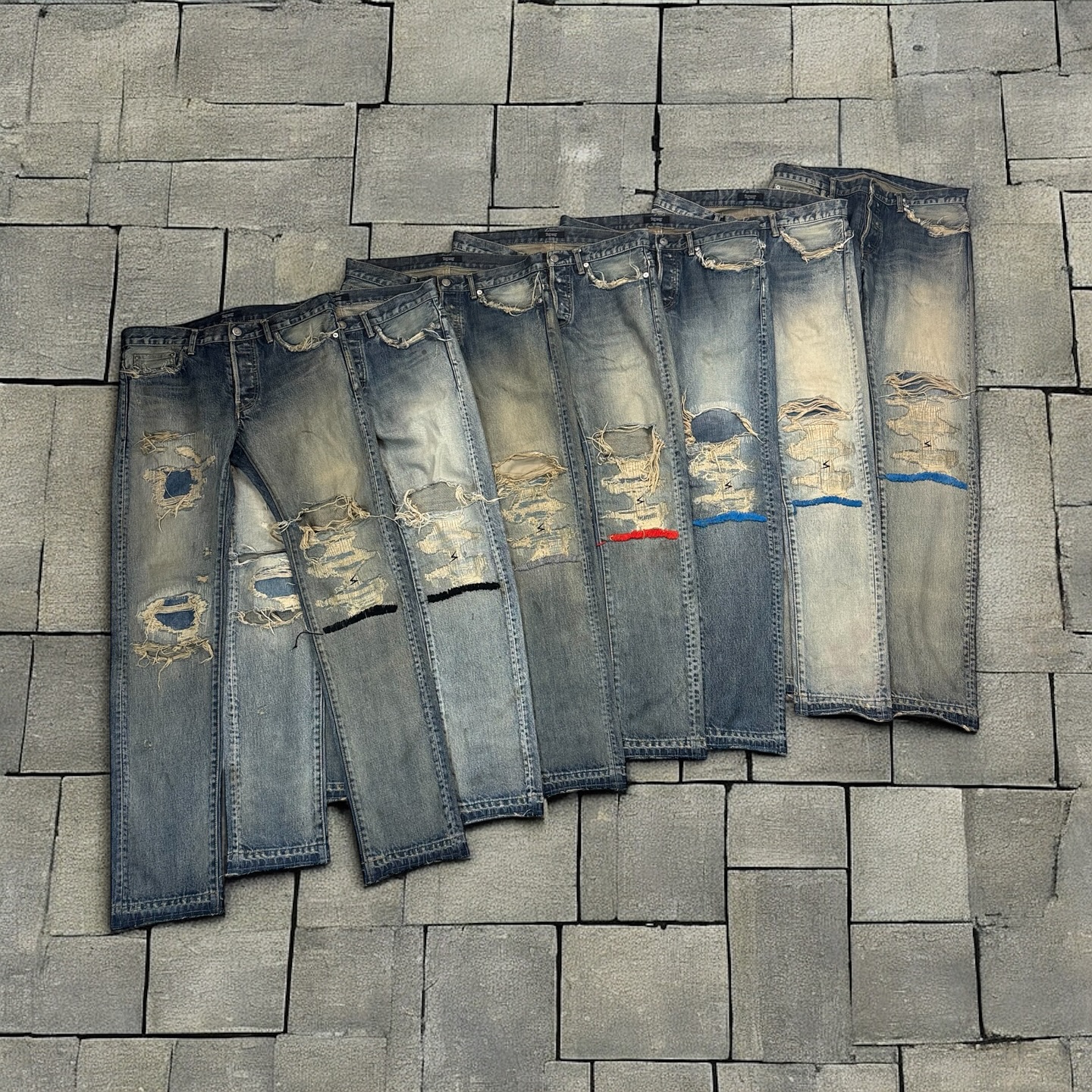 Rows of distressed denim jeans arranged on a tiled wall